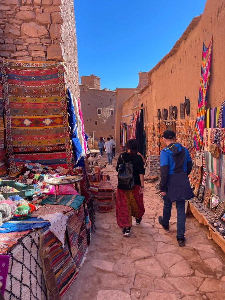 Viajes de compras a Marrakech Calle de zoco en Marrakech con puestos de artesanía y alfombras.