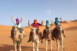 Grupo en camello posando con las manos en el aire en Marrakech